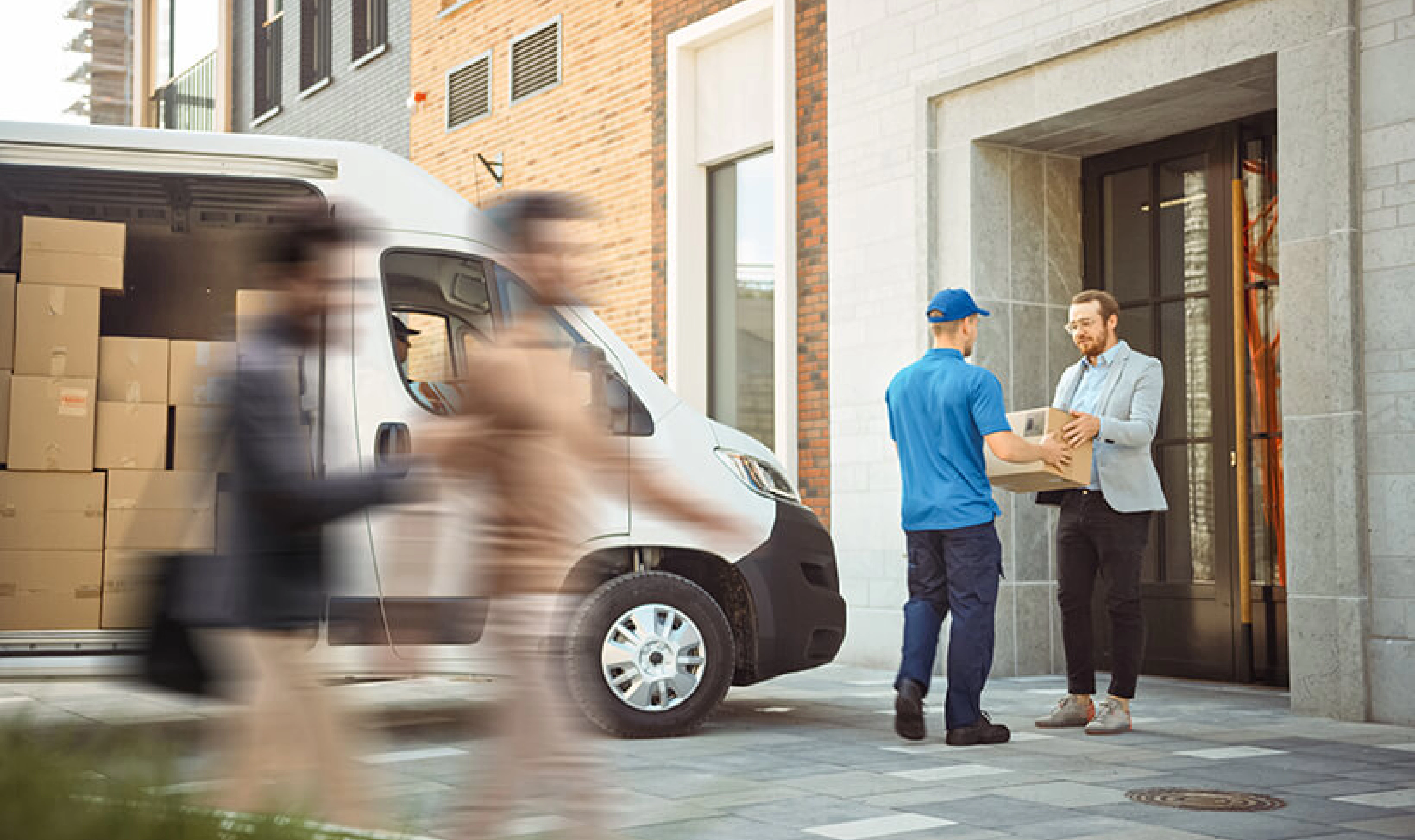 A person handing a box to a person in front of a building.