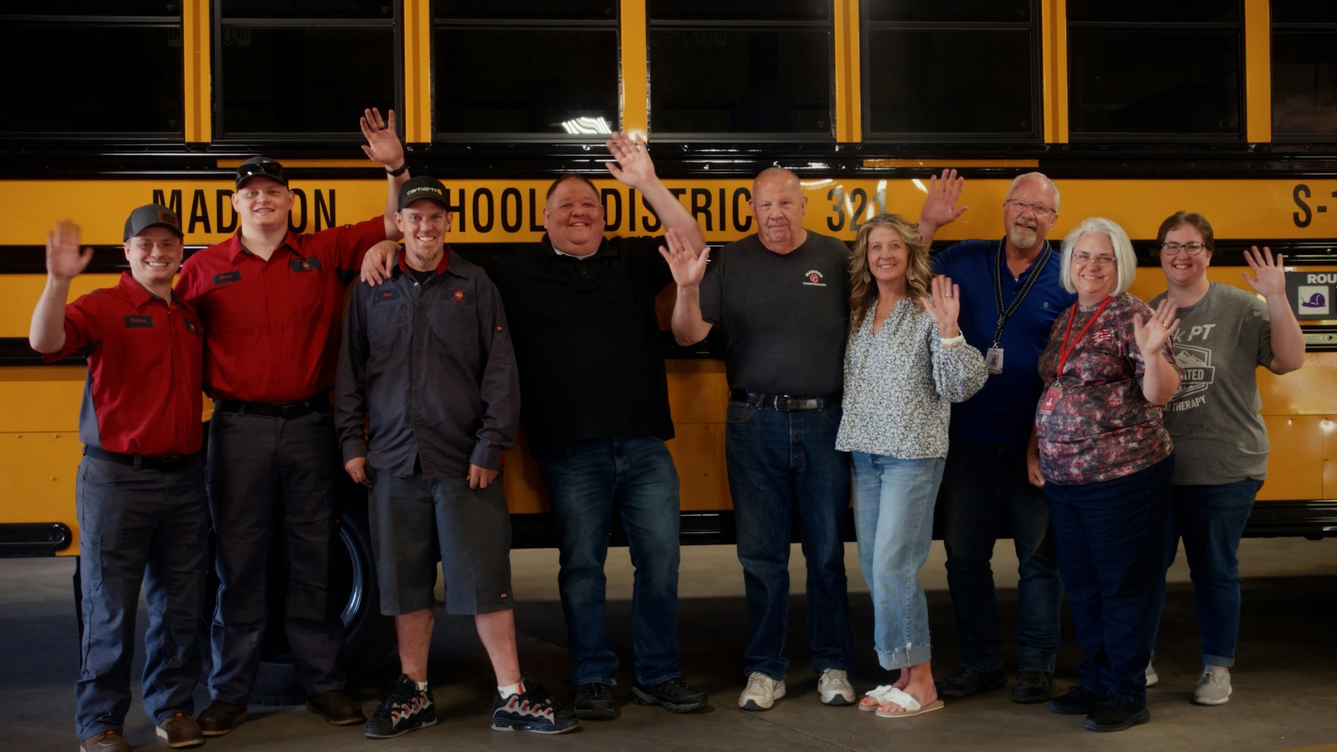 People standing in front of school bus waving.